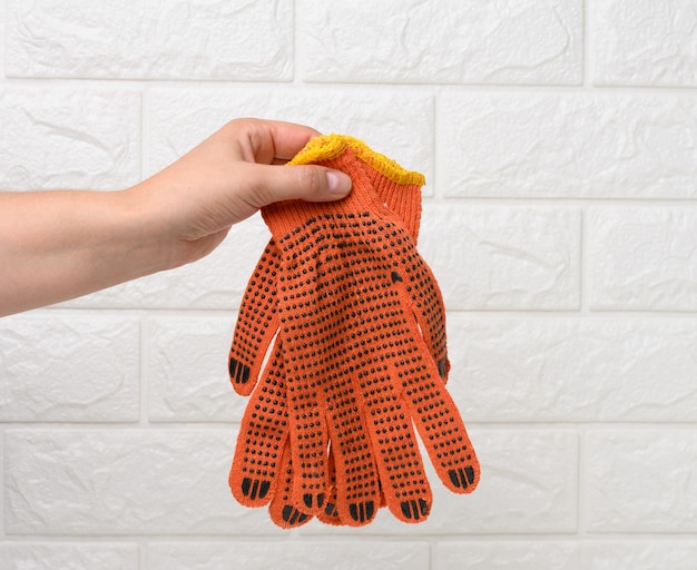 Weibliche Hand hält textile orange Arbeitshandschuhe auf weißem Hintergrund. Schutzkleidung für Arbeiter, Nahaufnahme