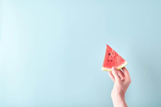 Weibliche Hand hält Wassermelonenscheibe auf blauem Hintergrund. Bunte heiße Sommerferien. Nahaufnahme von Wassermelonenscheiben in den Händen. Banner. Attrappe, Lehrmodell, Simulation.