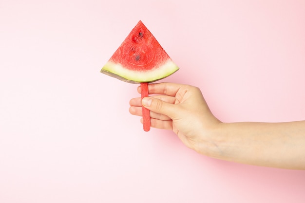 Weibliche Hand hält Wassermelonenscheibe auf Rosa.