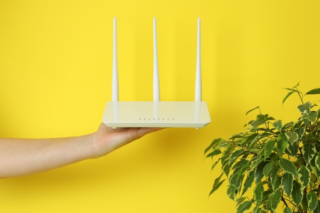 Weibliche Hand hält WLAN-Router auf gelbem Hintergrund