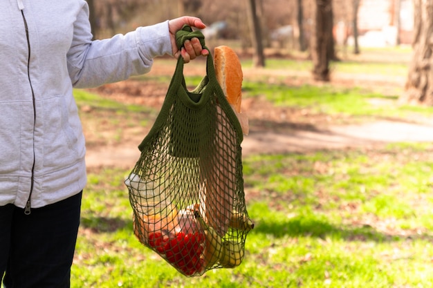 Weibliche Hand halten grüne Öko-Baumwoll-Stringtasche mit Bio-Lebensmitteln.