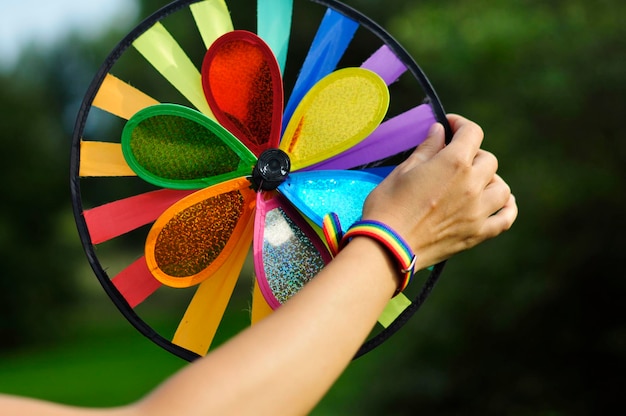 Foto weibliche hand in einem regenbogen-lgbt-armband dreht eine spielzeugwindmühle