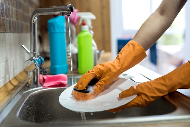 Weibliche Hand in Handschuhen beim Abwasch über der Spüle in der Küche. Hausarbeit