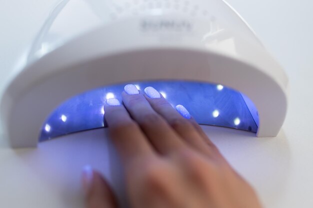 Weibliche Hand in trocknender UV-Lichtmaschine im Nagelstudio