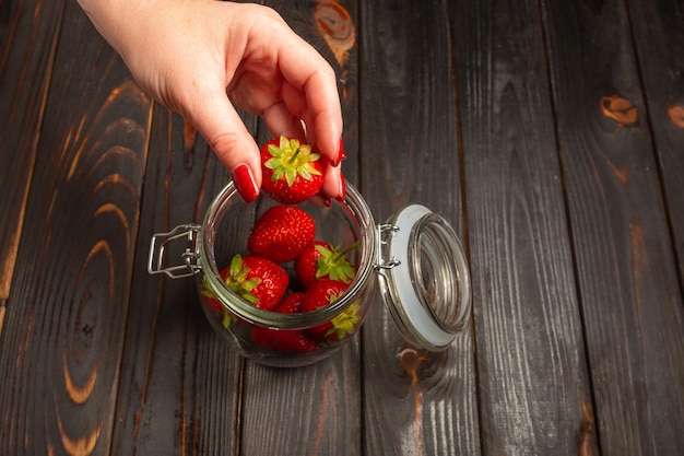 Weibliche Hand legt frische Erdbeeren in ein Glasgefäß