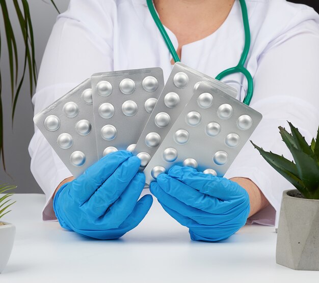 Weibliche Hand mit blauen sterilen Handschuhen hält einen Stapel Pillen in einer Blase