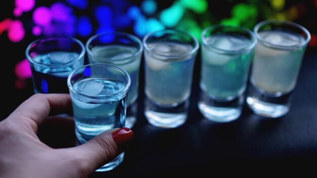 Weibliche Hand mit einem Schuss Alkohol, Neon verschwommener Hintergrund in der Bar