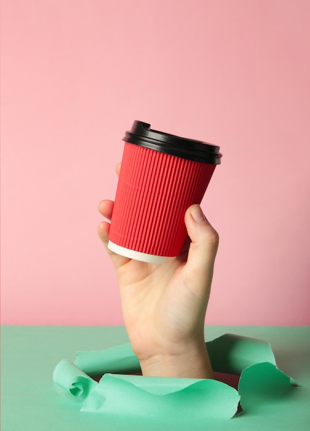 Weibliche Hand mit einer Tasse Kaffee, die durch das rosa Papier stanzt