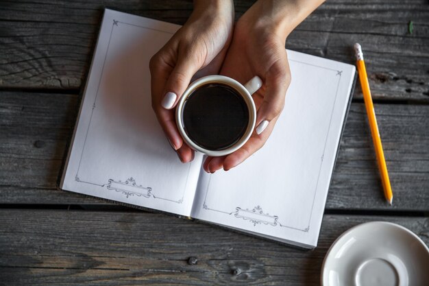 Weibliche Hand mit einer Tasse Kaffee, Notizen machend. Es funktioniert Aufzeichnungen. Geschäft