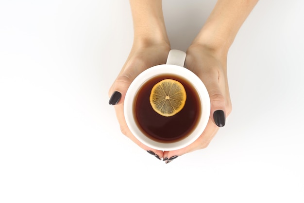 Weibliche Hand mit einer Tasse Tee mit Zitrone auf einer weißen Tischplatte