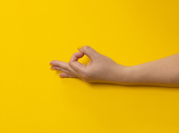 Weibliche Hand mit heller Maniküre zeigt OK-Zeichen auf gelbem Hintergrund