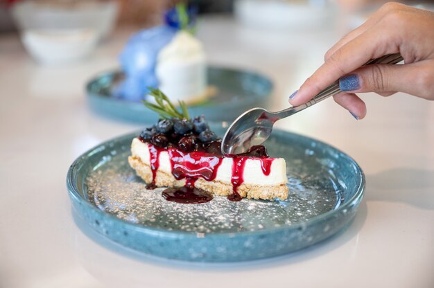 Weibliche Hand mit Löffel schneiden Blaubeer-Käse-Torte auf Keramikplatte