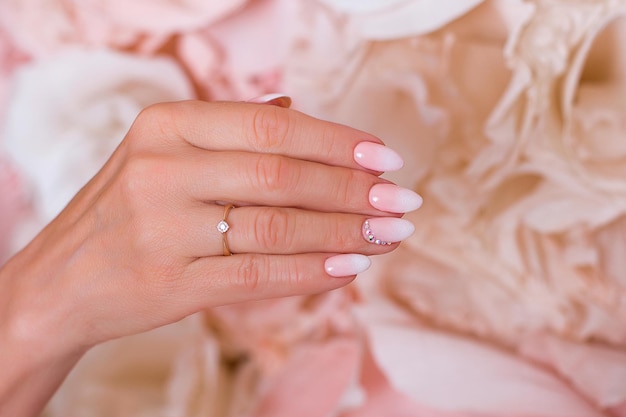 Weibliche Hand mit Ombre-Maniküre nagelt rosa Gelpolitur auf Papierblumenhintergrund