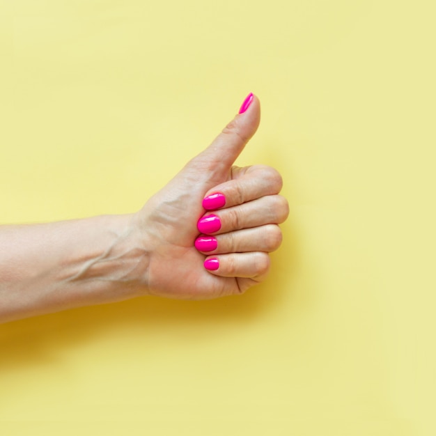 Weibliche Hand mit rosa Nagel auf Gelb.