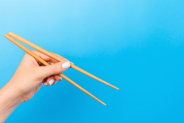 Weibliche Hand mit Stäbchen auf blauem Hintergrund. Traditionelles asiatisches Essen