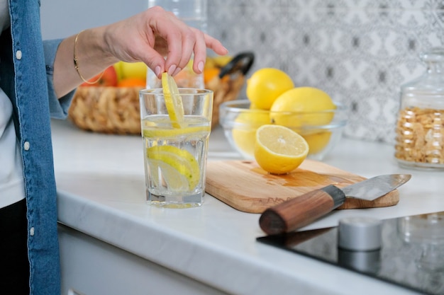 Weibliche Hand mit Zitronenscheibe in der Küche, mit frisch gemachtem Getränk Sprudelwasser mit Zitrone