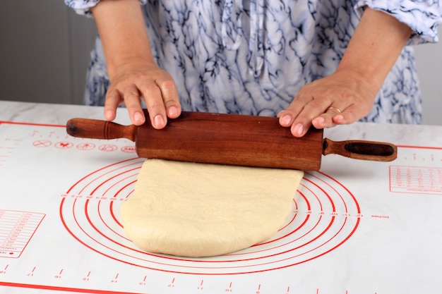 Weibliche Hand rollen Brotteig mit Holznudelholz aus, Backvorbereitung in der Küche