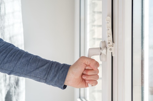 Weibliche Hand schloss ein modernes weißes PVC-Fenster mit einer angebrachten Befestigungsvorrichtung zur Belüftung