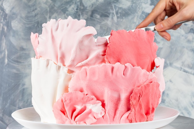 Weibliche Hand schneidet Stück appetitlichen Kuchen, der mit farbigem Mastixmesser auf grauem Hintergrund verziert ist