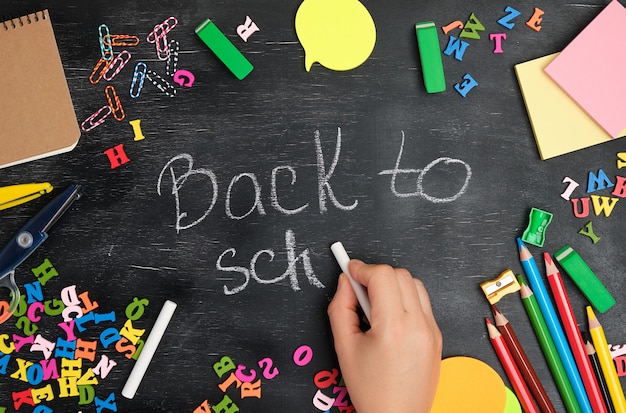 Weibliche Hand schreibt mit einer weißen Kreide auf eine Tafel zurück zu Schule