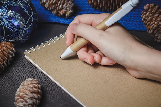 Weibliche Hand, Stift, Notizbuch, auf dem Weihnachtsdekorationshintergrund