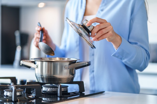Weibliche Hausfrau, die Stahlmetall-Topf für die Zubereitung des Abendessens in der Küche zu Hause verwendet. Küchenutensilien zum Kochen