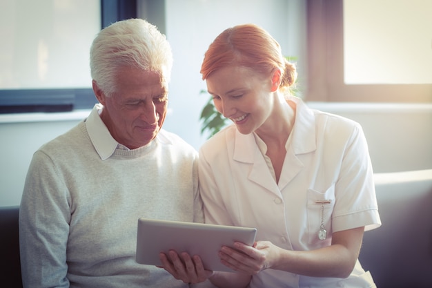 Weibliche Krankenschwester, die dem älteren Mann ärztlichen Attest über digitale Tablette zeigt