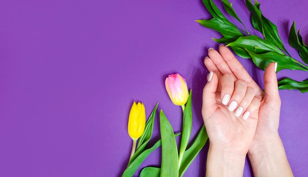 Weibliche Maniküre auf einem hellen Hintergrund. Lila Hintergrund mit Blumen. Banner.