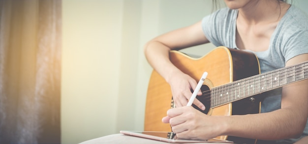 Weibliche Musiker spielen Gitarre und schreiben Songs mit dem Tablet