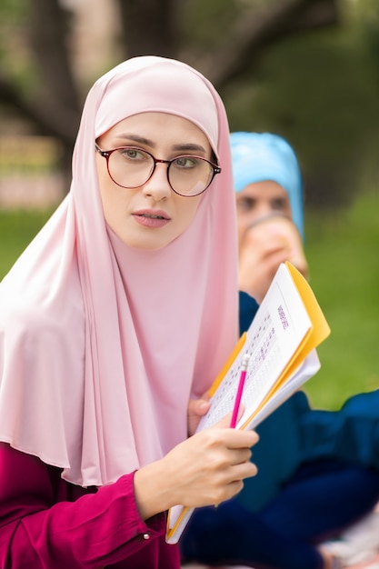 Foto weibliche muslimische studenten. weibliche muslimische studenten tragen helle hijabs und lernen zusammen draußen sitzen