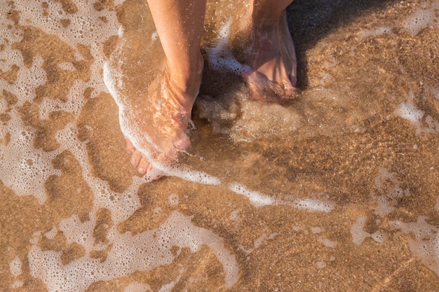 Weibliche nackte Füße stehen im Meer an einem Sandstrand Draufsicht flach gelegt