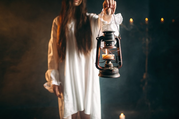 Weibliche Person im weißen Hemd hält Petroleumlampe in der Hand. Ritual der dunklen Magie, Okkultismus und Exorzismus