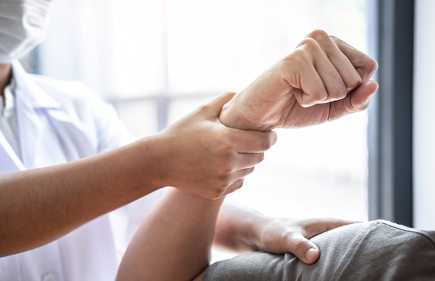 Weibliche Physiotherapeutin, die die Behandlung des verletzten Arms des männlichen Athleten des Athleten, das Dehnen und das Training untersucht, die Schmerzen der Rehabilitationstherapie in der Klinik macht.