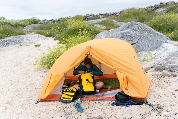 Weibliche Radfahrerreisende in einem Zelt, die ihre Kleidung organisieren und am Strand kostenlos campen?