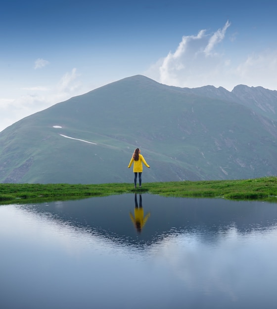 Weibliche Reisende in einer gelben Jacke steht am Ufer eines Sees schöne Spiegelung im Wasser