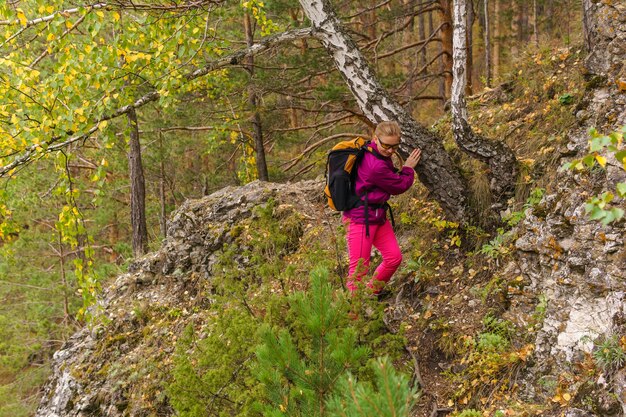 Weibliche Reisende mit Rucksack begeben sich vorsichtig auf einen Bergpfad durch den Herbstwald