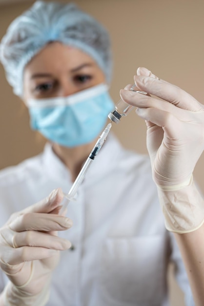 Weibliche Ärztin und Krankenschwester in voller medizinischer Uniform bereiten eine Spritze mit Medikamenten für den isolierten Impfstoff vor