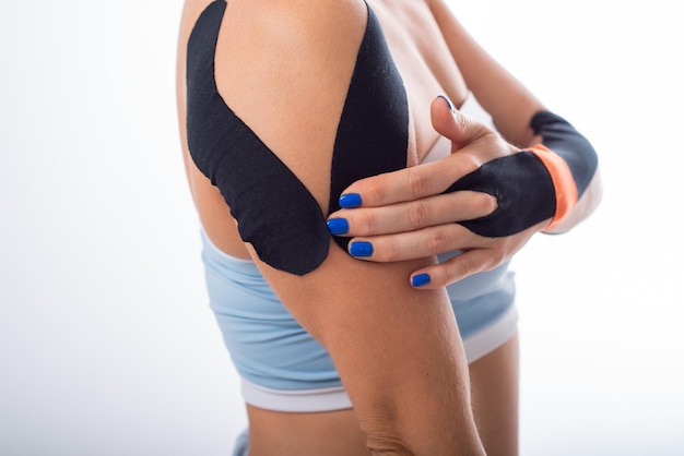 Weibliche Schulter mit Kineziotape auf weißem Hintergrund Alternative Medizin für Sportverletzungen von Gelenken und Bändern Junge Sportlerin mit Krankenakte an schmerzender Schulter und Handgelenk