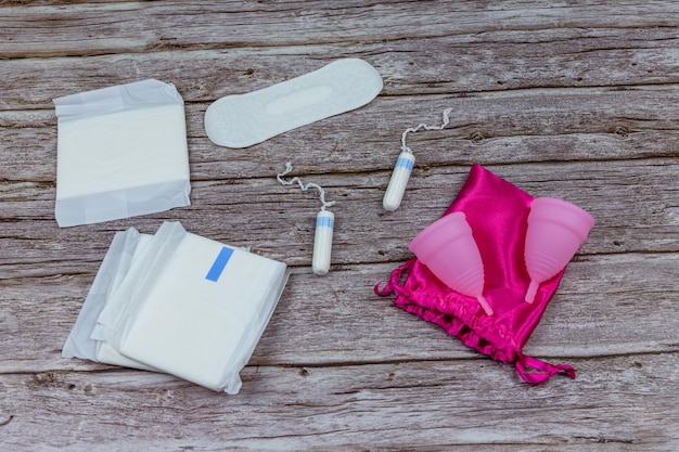 Weibliche Tampons, Menstruationstasse und Damenbinden auf Holzhintergrund Frauenhygiene