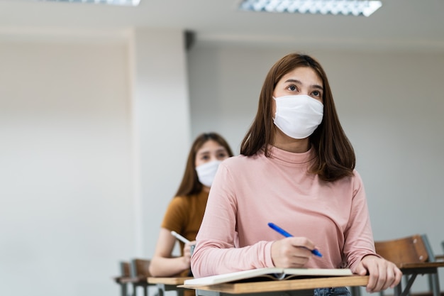 Weibliche Teenager-Studenten tragen Gesichtsmaske und halten Abstand, während sie im Klassenzimmer und auf dem College-Campus studieren, um eine COVID-19-Pandemie zu verhindern