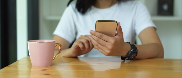 Weibliche Teenagerhände, die Smartphone auf Holztisch mit einer Tasse Getränk verwenden