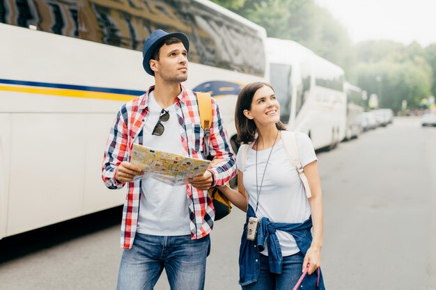 Weibliche und männliche Touristen, die nahe Bussen, Karte in den Händen halten, beim Suchen nach Hotel gehen, wo man bleibt. Energetische Reisende auf der Suche nach einem Ort an einem unbekannten Ort. Menschen, Explorationskonzept