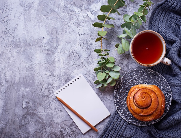 Weiblicher Arbeitsplatz mit Brötchen, Tasse Tee und Notizbuch. Flache Lage, Draufsicht