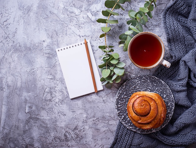 Weiblicher Arbeitsplatz mit Brötchen, Tasse Tee und Notizbuch