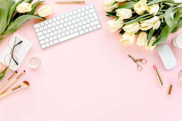 Weiblicher Arbeitsplatz mit Computer-Tulpenblumenstrauß, goldenem Accessoires-Tagebuch auf rosa Hintergrund