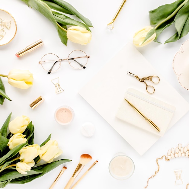 Weiblicher Arbeitsplatz mit gelber Tulpe blüht Damenmode goldene Accessoires Tagebuchbrille auf weiß