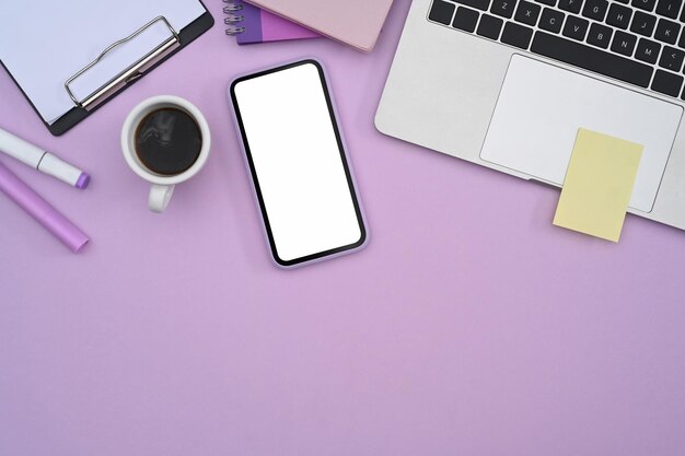 Weiblicher Arbeitsplatz mit Smartphone-Laptop-Computer und Schreibwaren auf violettem Hintergrund