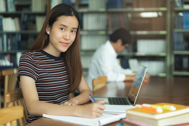 Weiblicher asiatischer studierender und lesebuch in der bibliothek