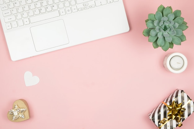 Weiblicher Bürodesktop mit Bürozubehör auf rosa Oberfläche. Damenarbeitsbereich mit Sukkulenten, Kerzen und Kosmetika.