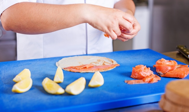 Weiblicher chef bereitet pfannkuchen mit lachsen und kaviar in der küche des restaurants zu